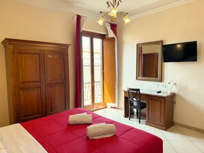 Una habitación de hotel con cama, escritorio, silla, televisor y armario.