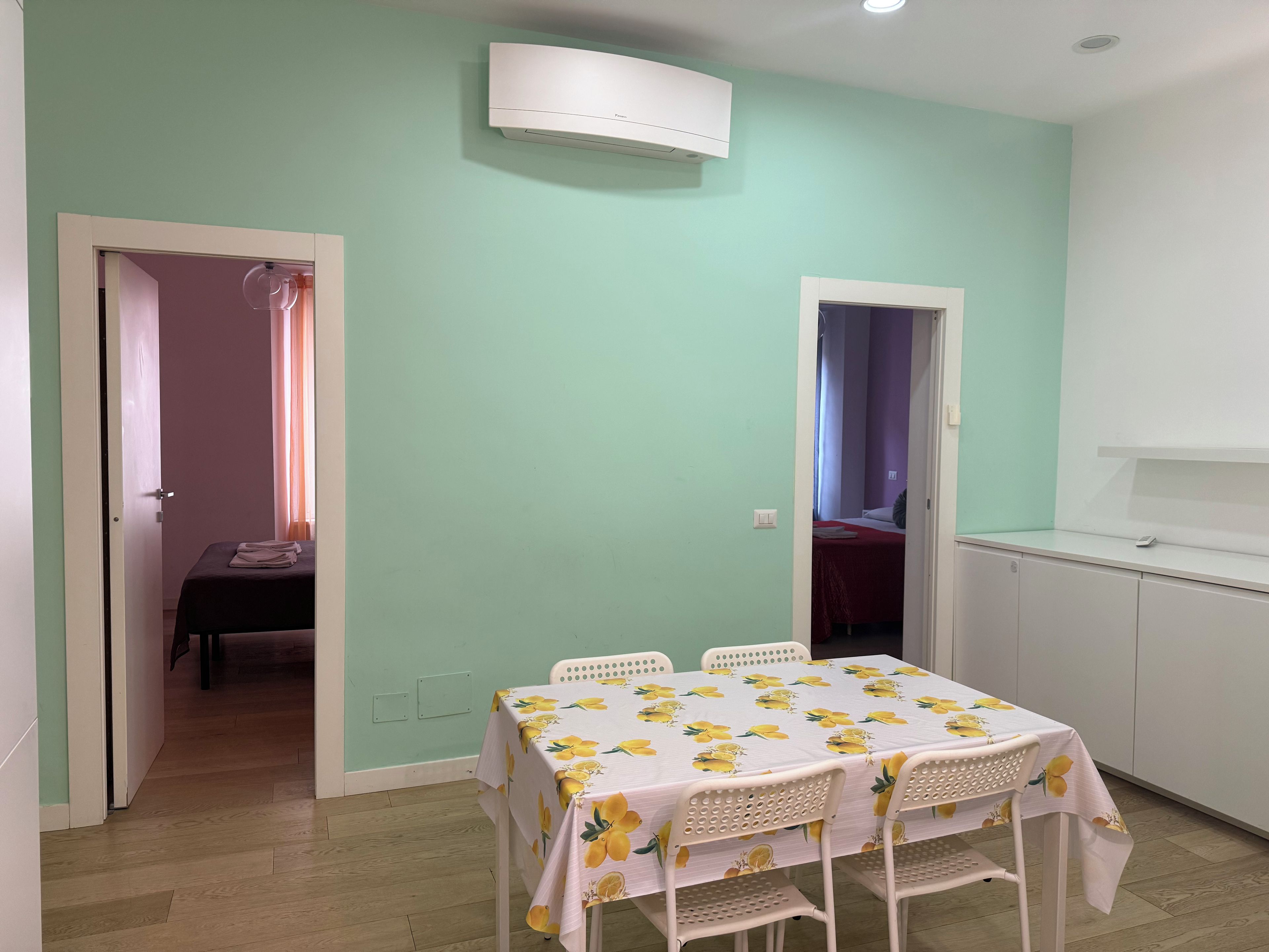 Une pièce comprenant une table dressée pour quatre personnes, un coin cuisine et une porte donnant sur une autre pièce.