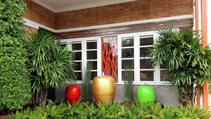 A variety of potted plants arranged in front of a window with a brick wall and a white-framed window. - Bander Hotel (Phu Khiao)