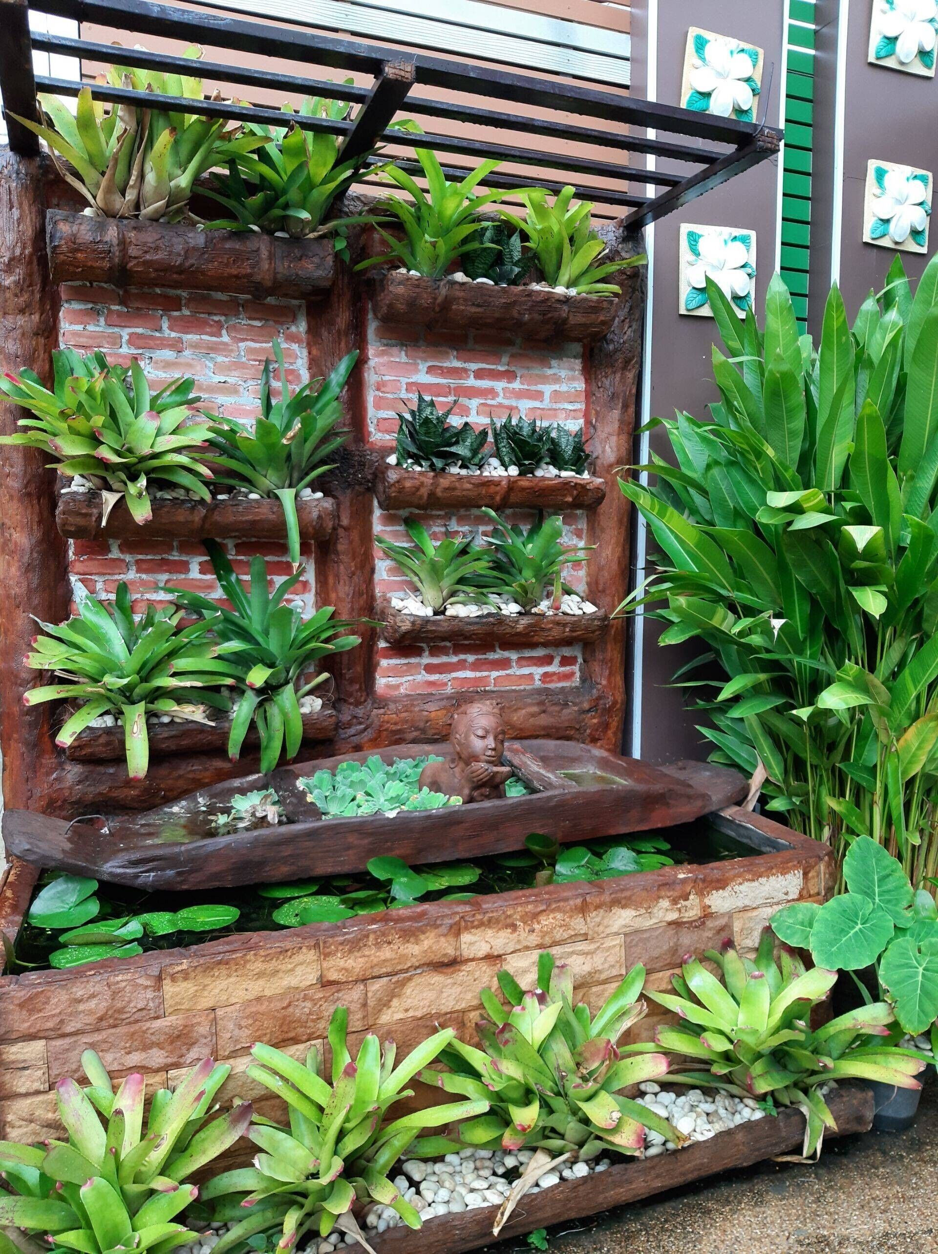 Un jardin où diverses plantes sont disposées sur des étagères en bois, adossées à un mur de briques.