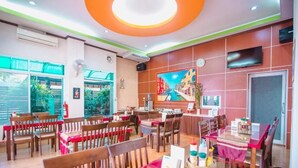 A restaurant with multiple tables and chairs, a television mounted on the wall, and a large window providing a view of the outdoors. - Bander Hotel (Phu Khiao)