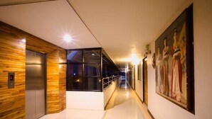 A modern hotel corridor with wooden paneling, an elevator, a glass-enclosed area, and a painting on the wall. - Bander Hotel (Phu Khiao)