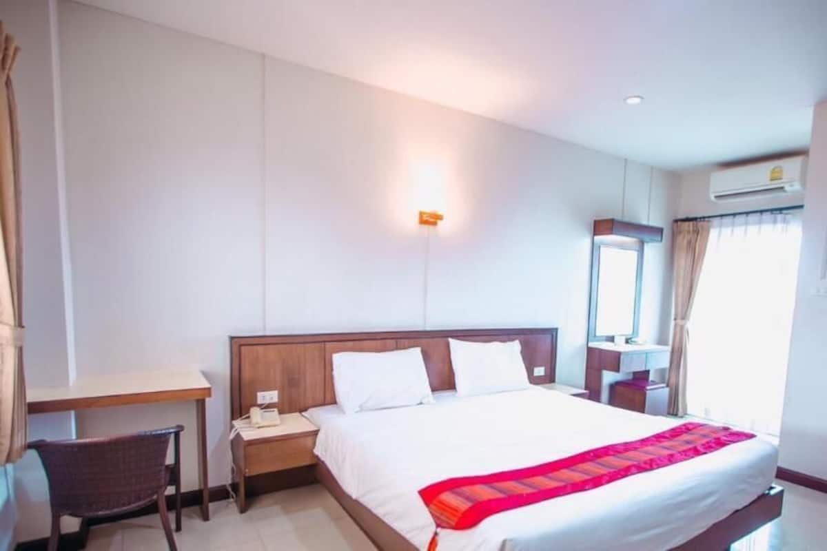A hotel room with a bed, a desk, a chair, a nightstand, and a mirror.
