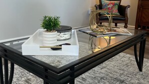 Ein modernes Wohnzimmer mit einem Glastisch, einem Blumentopf, einer dekorativen Ablage und einer Lampe.