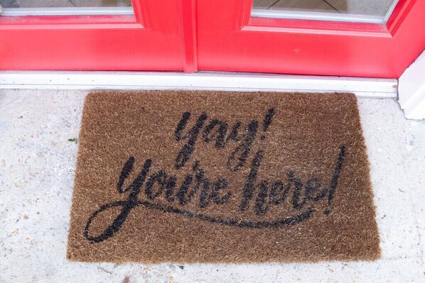 A brown doormat with the text "Yay! You're here!" on a white door.