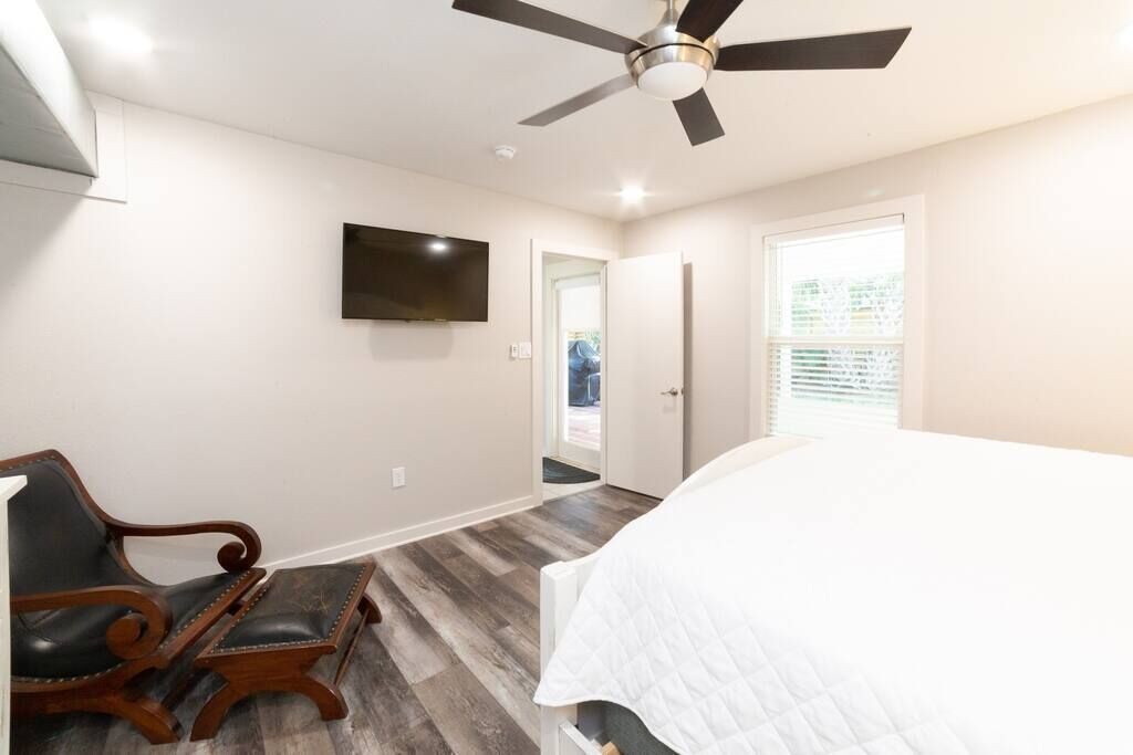 A bedroom with a bed, a ceiling fan, a TV mounted on the wall, and a door leading to another room.
