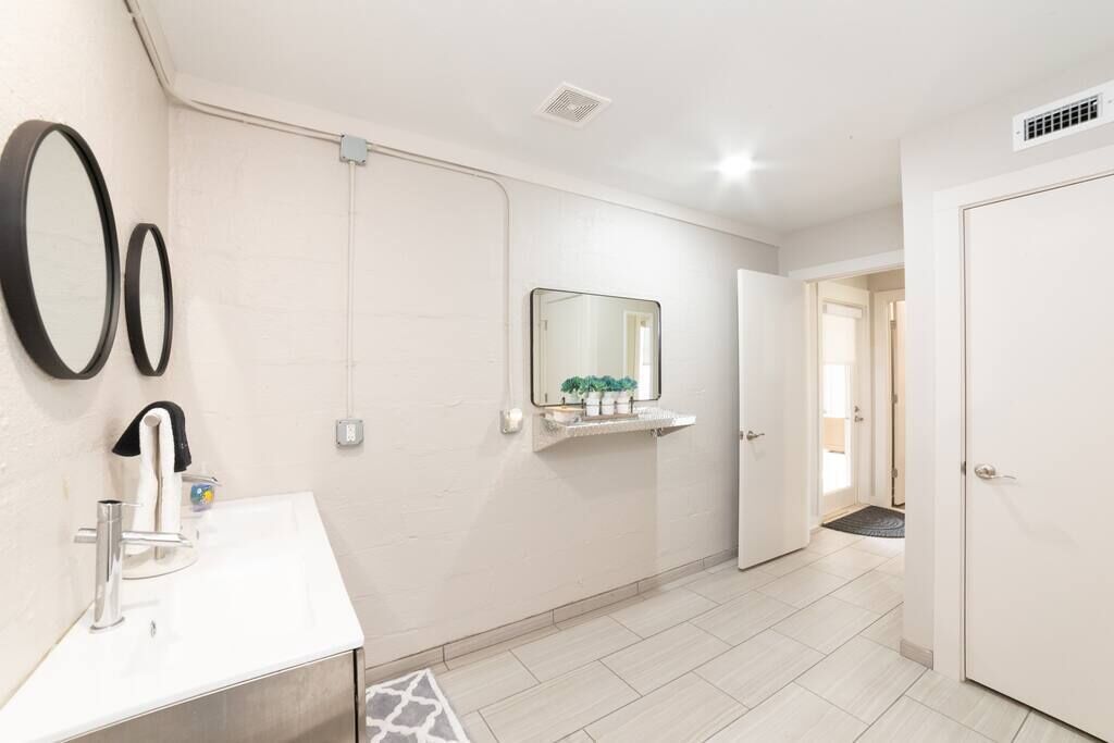 Een moderne badkamer met een witte wasbak, twee spiegels, een handdoekhouder en een klein plankje met toiletartikelen.
