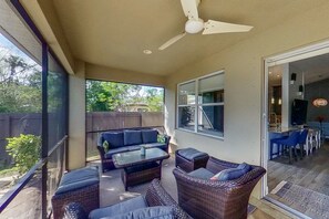 Relax in a shaded outdoor space with wicker sofas and chairs, a glass table, and a view of lush greenery.