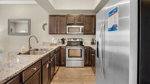 A kitchen with a stainless steel refrigerator, a microwave, and a double oven. There is a sink with a faucet, and wooden cabinets.