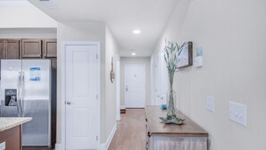 A kitchen with a stainless steel refrigerator, wooden cabinets, and a countertop. There is a hallway with a door leading to another room.