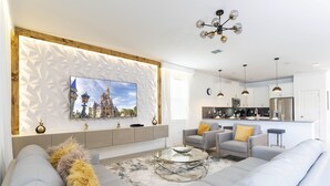 A modern living room with a sofa, a glass coffee table, and a TV mounted on a textured wall. - Grand Opening! 9BD/5BA-Storey Lake Resort/Lake View/GameRoom (Kissimmee)