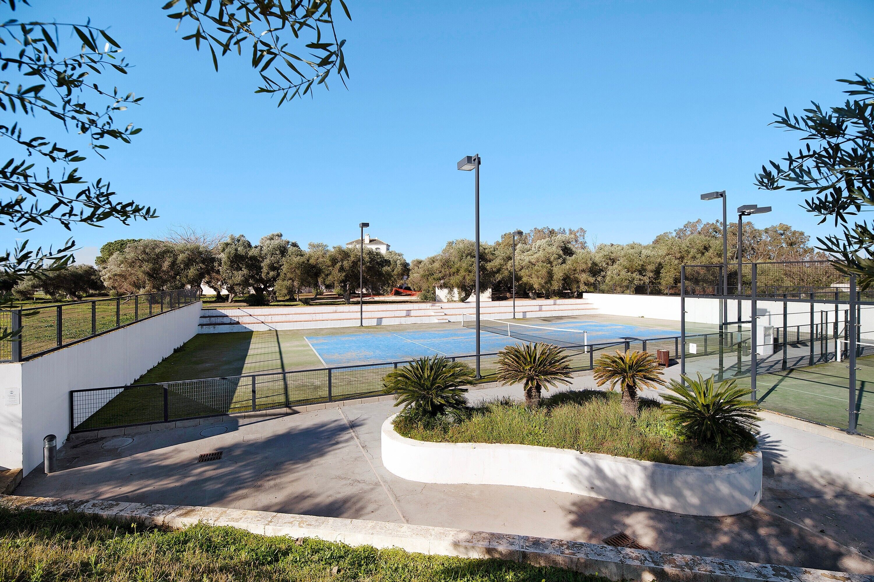 A tennis court with surrounding greenery and a white building.