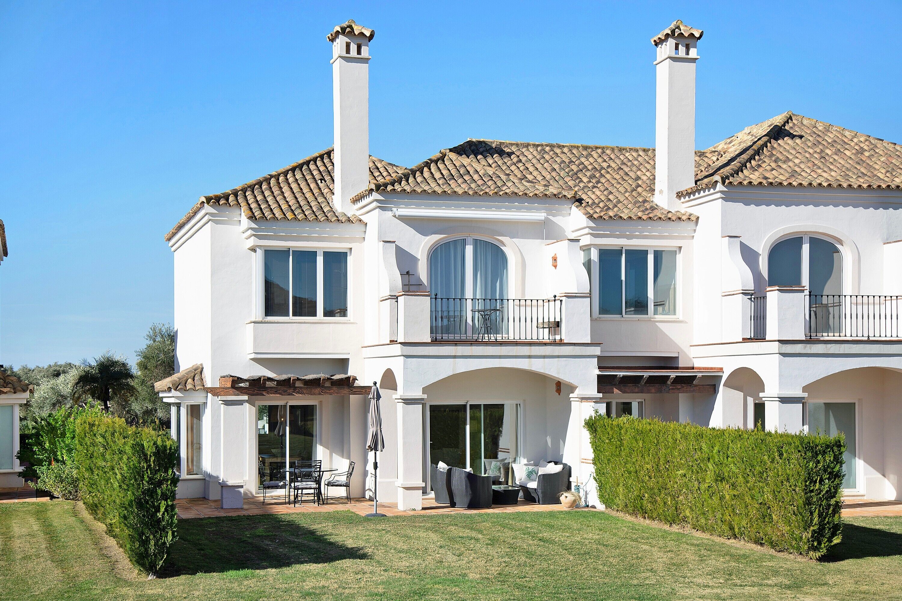 A multi-story house with a tiled roof, large windows, and a well-maintained lawn.