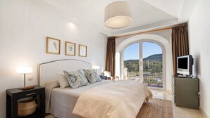 Ein Schlafzimmer mit Bett, Nachttisch, Lampe, Fernseher und Blick ins Freie.