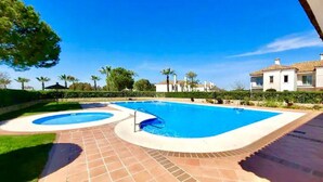 Ein Schwimmbecken mit zwei separaten Bereichen, umgeben von einer gefliesten Terrasse und einem gepflegten Rasen.
