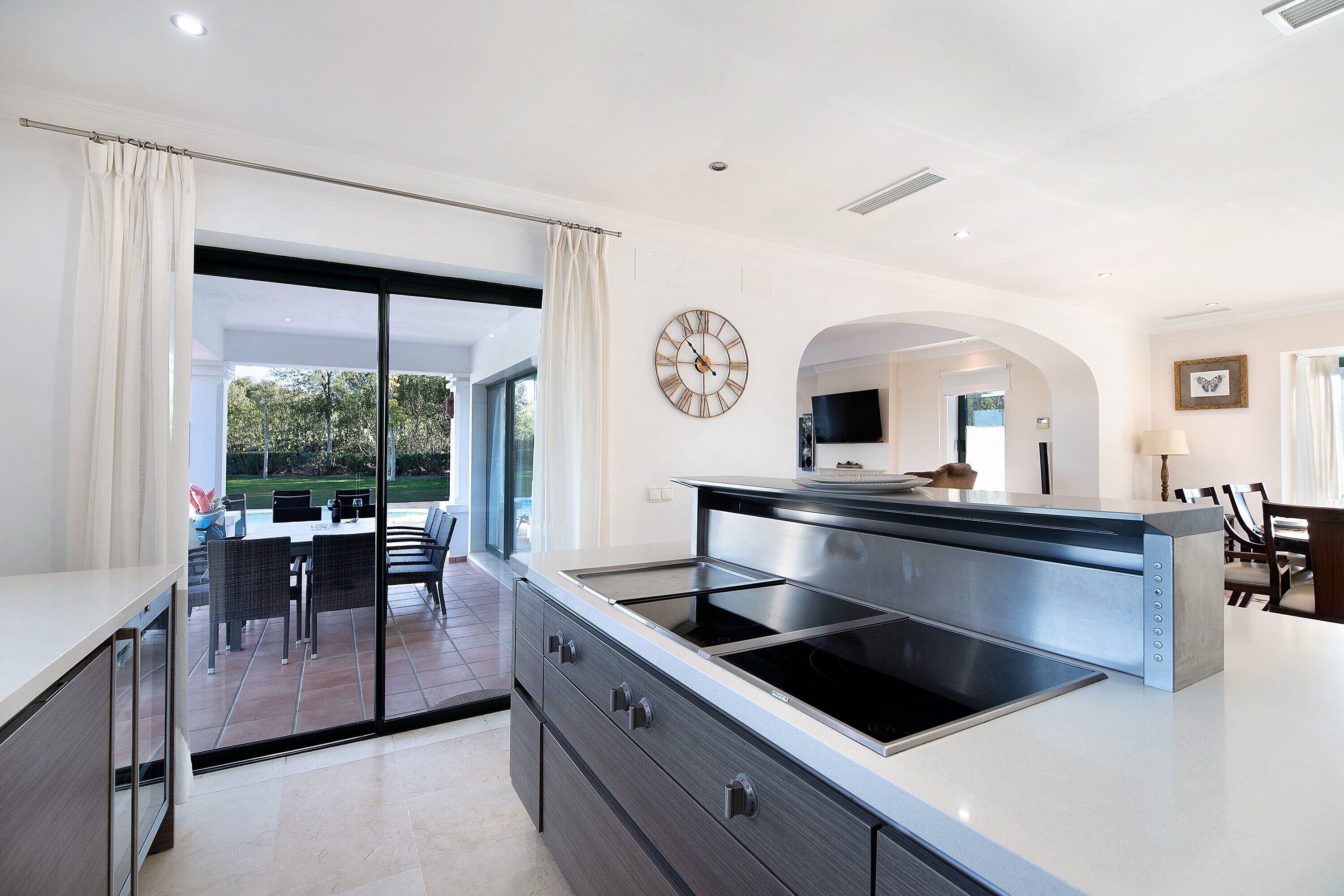 Una cocina moderna con una isla grande, puertas de cristal correderas a un patio y un comedor con sillas.