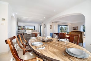 Un espace repas comprenant une table ronde, des chaises et donnant sur la cuisine et l’extérieur.
