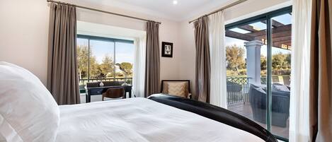 A hotel room with a large bed, a desk, and a balcony with outdoor furniture.