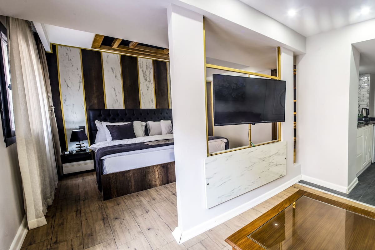 Une chambre d’hôtel moderne comprenant un lit, une télévision, un petit coin cuisine et un espace de vie avec un canapé.