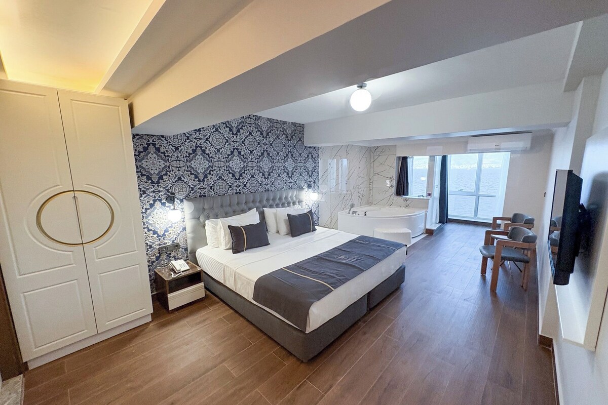 Un dormitorio moderno con una cama grande, una bañera integrada y una zona de estar con vistas al mar.