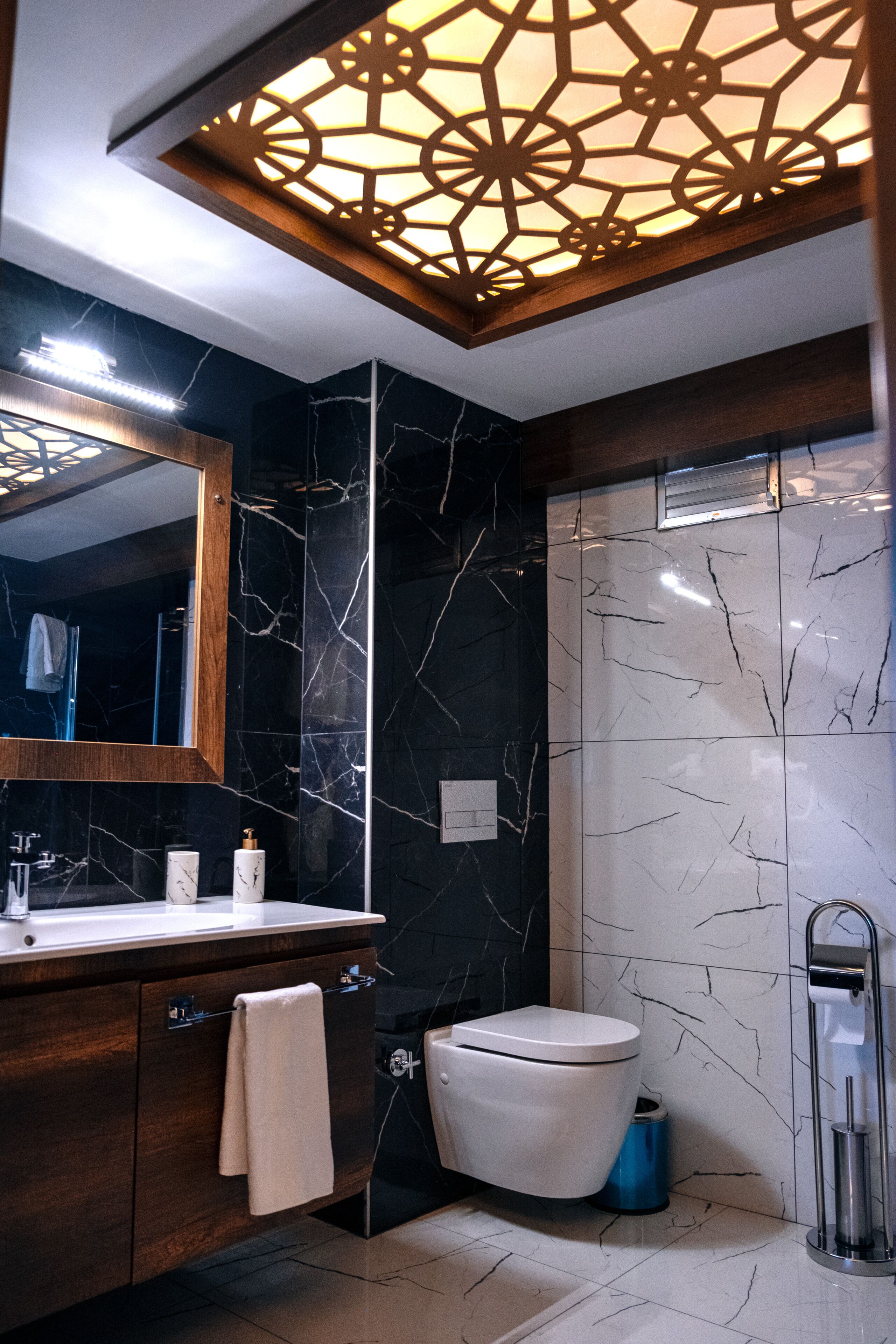 A modern bathroom with a marble backsplash, a wooden vanity, a toilet, and a shower area.