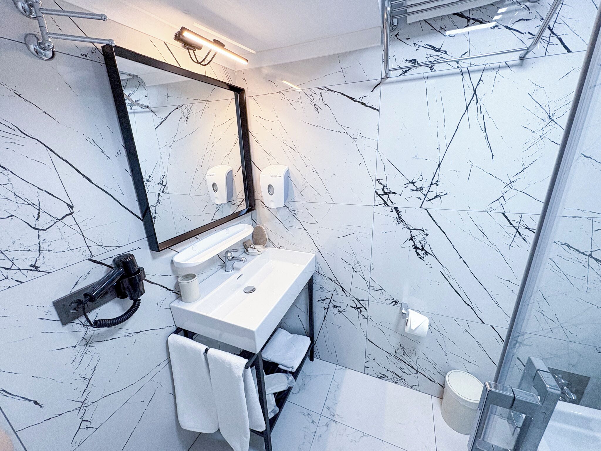A modern bathroom with a white sink, a large mirror, and a glass shower enclosure.
