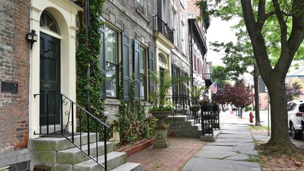 A row of townhouses with a brick facade, a green door, and a small garden area with a planter.