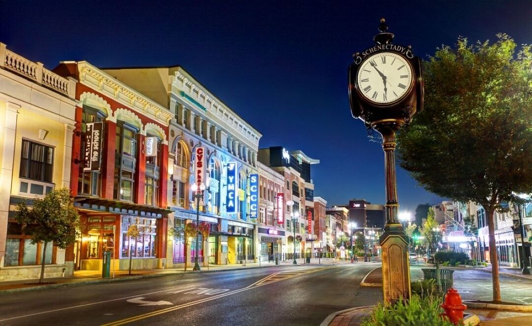 Una calle nocturna con edificios iluminados, un reloj destacado y un hidrante rojo.