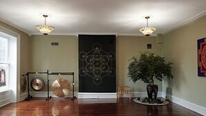 A spacious room with hardwood floors, a large abstract painting on the wall, a potted plant, and a music stand with instruments.