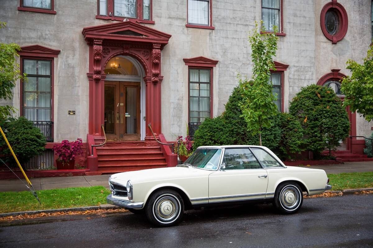 A classic white car parked in front of a building with a red entrance and steps.