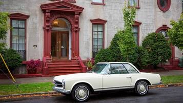 A classic white car parked in front of a building with a red entrance and steps.