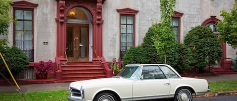 Un coche blanco clásico estacionado frente a un edificio con entrada roja y escalones.