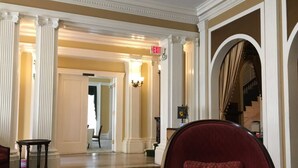A spacious lobby with a red armchair, a patterned carpet, and classical architecture including columns and an archway.
