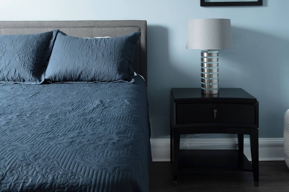 A bedroom with a bed, a nightstand, a lamp, and a framed picture on the wall.