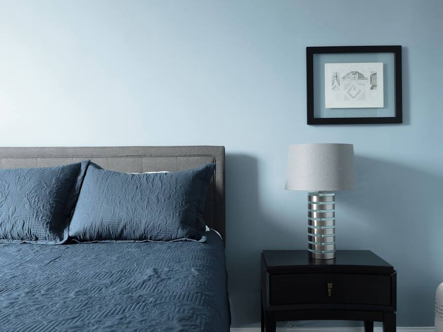 A bedroom with a bed, a nightstand, a lamp, and a framed picture on the wall.