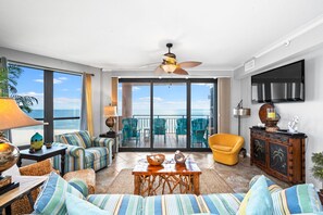 A spacious living room with a balcony overlooking the ocean, featuring a ceiling fan, a television, and a wooden cabinet. - Updated condo w/ beautiful OCEAN views @ the Desirable SEA CHASE condominiums!  (Orange Beach)
