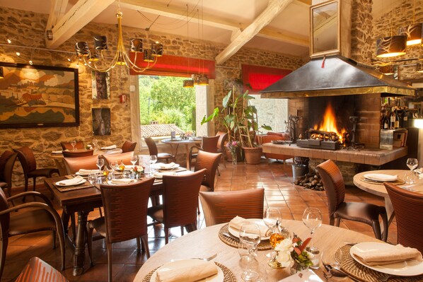 A restaurant with stone walls, wooden furniture, and a fireplace. Tables are set with plates, glasses, and cutlery.