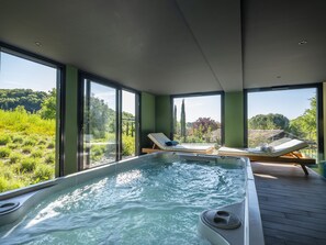 A modern spa area with a hot tub, two lounge chairs, and large windows offering a view of a lush landscape.