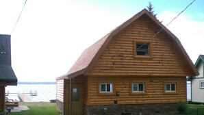 Uma cabana de tronco com fundação de pedra, um deck de madeira e vista para a água.