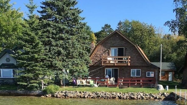 Uma cabana com varanda voltada para um lago, rodeada por árvores.