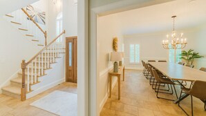 Un comedor amplio con una larga mesa y sillas, un candelabro y una escalera que lleva a otra habitación.