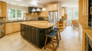 Una cocina amplia con una isla grande, armarios de madera y electrodomésticos de acero inoxidable, además de iluminación colgante.