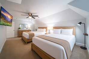 Une chambre d’hôtel moderne équipée de deux lits, d’un ventilateur de plafond, d’un téléviseur à écran plat, d’un bureau avec un miroir et d’une table de chevet avec une lampe.