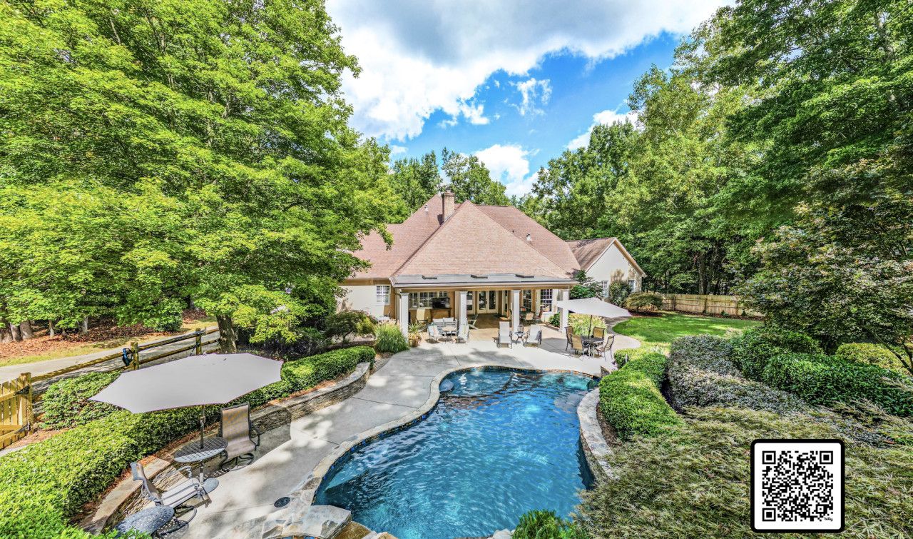 A house with a swimming pool, surrounded by lush greenery and a wooden fence.
