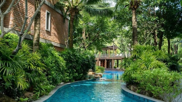 A pool surrounded by lush greenery and a wooden building. - The Title Naiyang Residence (Sa Khu)