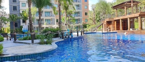 A swimming pool surrounded by palm trees and a multi-story building with balconies.