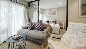 A modern bedroom with a large bed, a sofa, a small table, and a mirror. - The Title Naiyang Residence (Sa Khu)