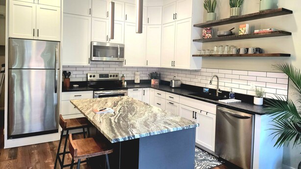 Una cocina moderna con armarios blancos, electrodomésticos de acero inoxidable, una isla de mármol y taburetes de madera.