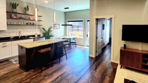 Una cocina moderna con una isla central, suelo de madera y un televisor de pantalla plana montado en la pared.