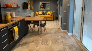 A modern kitchen with a dining area, a yellow sofa, and a large sliding glass door. - Fabulous apartment for 2 in Llansteffan (Llansteffan)